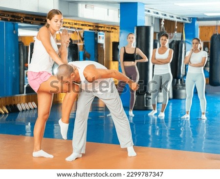 Concentrated girl performing knee kick with wristlock to male opponent while sparring during self defence training in gym