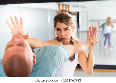 Concentrated girl practicing effective self defence techniques with coach in training room, using palm to launch blow in chin..