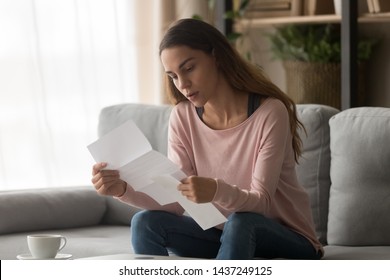 Concentrated girl sit on couch holding paper document in hands reading carefully examining, focused millennial woman study received letter, check post paperwork correspondence in living room - Shutterstock ID 1437249125