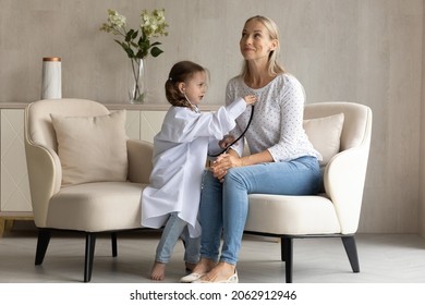 Concentrated happy adorable small child daughter in medical uniform listening heartbeat of beautiful cheerful young mother, playing interesting doctor patient game on weekend in modern living room. - Powered by Shutterstock