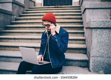 Concentrated hipster blogger searching information on websites and working on publication at modern laptop device with wireless internet on street.Pensive student watching design tutorial on netbook - Shutterstock ID 1064508284