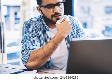 Concentrated hipster guy watching tutorial on laptop computer studying on online courses while sitting in cafe interior,contemplative graphic designer analyzing project information doing remote job - Powered by Shutterstock