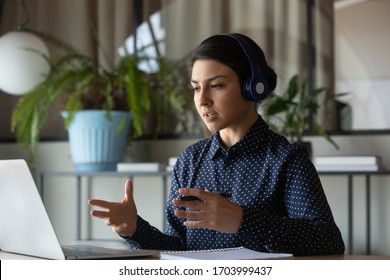 Concentrated Indian Female Employee In Wireless Earphones Talk On Video Call Using Modern Laptop, Ethnic Woman Worker In Headphones Have WebCam Conversation Or Conference, Consult Client Online