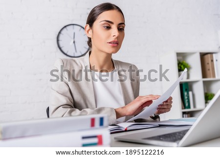 concentrated interpreter working with document near laptop and dictionaries on blurred foreground