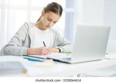 Concentrated latin teenage girl making notes in her notepad, using laptop while having online lesson at home - Powered by Shutterstock