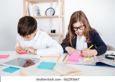 Concentrated little boy and girl sitting and writing on colorful sticky notes at the table - Powered by Shutterstock