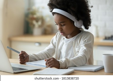 Concentrated Little Cute African American Small Child Girl In Modern Wireless Headphones Sitting In Front Of Computer, Checking Tasks At Online School Class, E-learning Distant Education Concept.