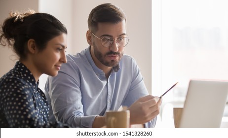 Concentrated male businessman looking at computer monitor, working with a young Indian female worker on a project, people holding a video meeting with a client or interviewing a job candidate.