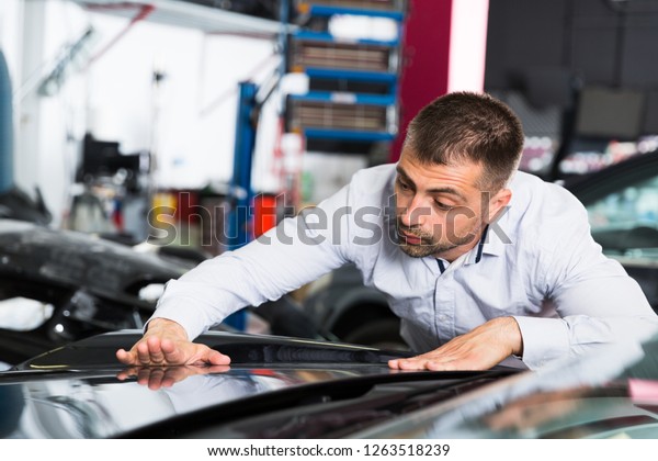 Concentrated male car owner\
touching surface repainted body, checking painting quality in car\
repair shop