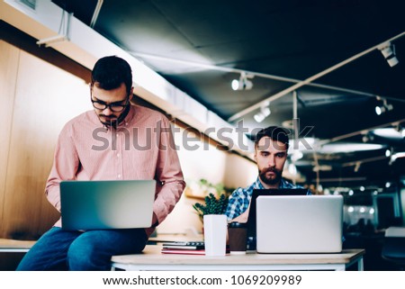 Concentrated male it developers working on laptop computers in office, searious young hipster guys programming new app for netbooks doing productive job for startup together in coworking space 