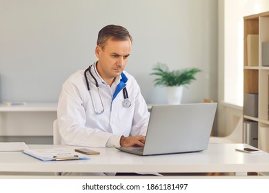 Concentrated Male Doctor Sitting In Office In Front Of Laptop And Reviewing Test Results For Disease. Doctor Is Dissatisfied With The Results Of The Tests And Worries About His Patient.