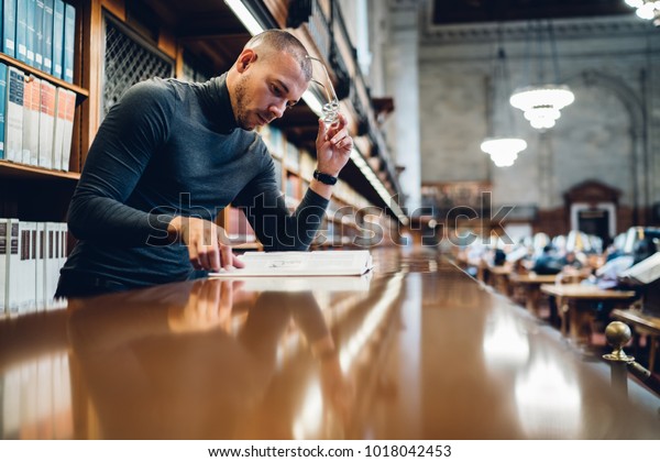 Concentrated male journalist analyzing content
of book making research for writing article, clever academic
professor learning in university library increasing knowledge in
nonfiction
literature