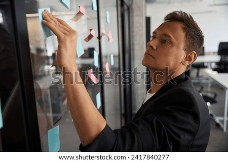 Concentrated man statistician writing down his ideas in the sticky notepad