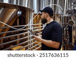 Concentrated man, technologist examining brewing equipment, maintaining thigh standards necessary for quality beer production. Concept of beer, brewery, manufacture, quality control