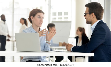 Concentrated man and woman workers sit at office desk negotiating using laptop discussing ideas, diverse colleagues talk brainstorming negotiate on business project together. Cooperation concept