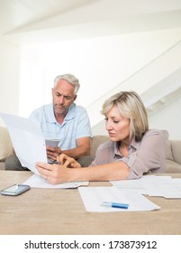 Concentrated Mature Man And Woman With Bills Sitting On Sofa At Home