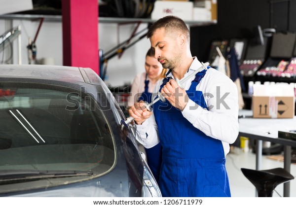 Concentrated mechanic performing car\
body repair at auto workshop with tools for repairing\
dents\
