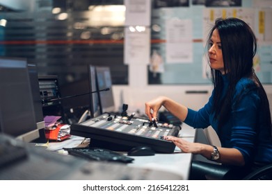 Concentrated Middle Aged Beautiful Woman Working On A Tv Station As A Producer In A Broadcast Control Room. Show Production Maker. Using Regulators On A Equipment In A Broadcast Room. Copy Space.