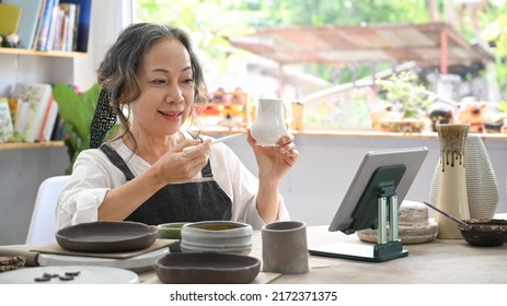 Concentrated Middle Aged Woman Painting Pottery Bowl In Workshop. Indoors Lifestyle Activity, Handicraft, Hobbies Concept