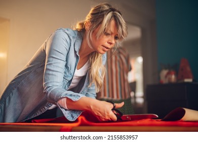 Concentrated Middle Aged Woman Tailor Cuts With Scissors Pattern Dress Detail On Sketch Lines For Sewing Machine. Workplace Of A Dressmaker. Handmade Concept. Portrait Of A Woman Tailor Working.