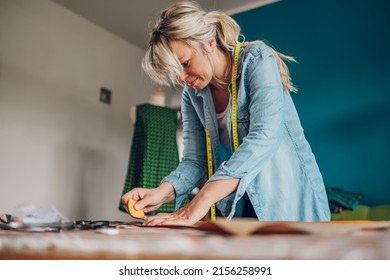 Concentrated Middle Aged Woman Tailor Using Scissors Pattern Dress Detail For Sketch Lines On Fabric For Sewing Machine. Workplace Of A Dressmaker. Handmade Concept. Focus On Woman Tailor Using Chalk