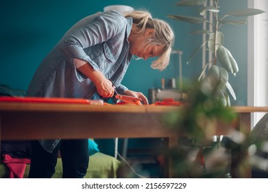 Concentrated Middle Aged Woman Tailor Cuts With Scissors Pattern Dress Detail On Sketch Lines For Sewing Machine. Workplace Of A Dressmaker. Handmade Concept.