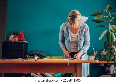 Concentrated Middle Aged Woman Tailor Cuts With Scissors Pattern Dress Detail On Sketch Lines For Sewing Machine. Workplace Of A Dressmaker. Handmade Concept. Portrait Of A Tailor Woman Working.