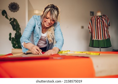 Concentrated Middle Aged Woman Tailor Using Chalk For Sketch Lines On Fabrics For Tailoring A Dress. Workplace Of A Dressmaker. Handmade Concept. Tailor Working At Home.