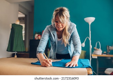 Concentrated Middle Aged Woman Tailor Cuts With Scissors Pattern Dress Detail On Sketch Lines For Sewing Machine. Workplace Of A Dressmaker. Handmade Concept.