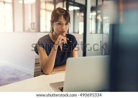 Concentrated middle aged woman working on her computer. Start-up office background
