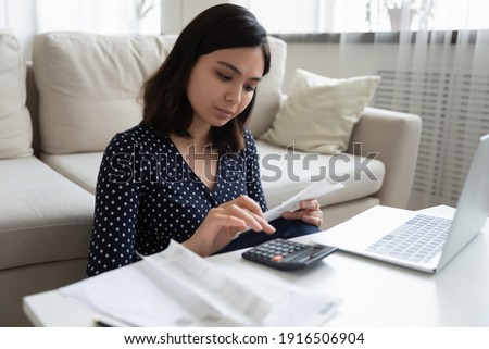 Concentrated millennial vietnamese female engaged in home banking using calculator and laptop. Attentive asian woman count taxes rental tenancy sum to pay online control accounts review utility bills