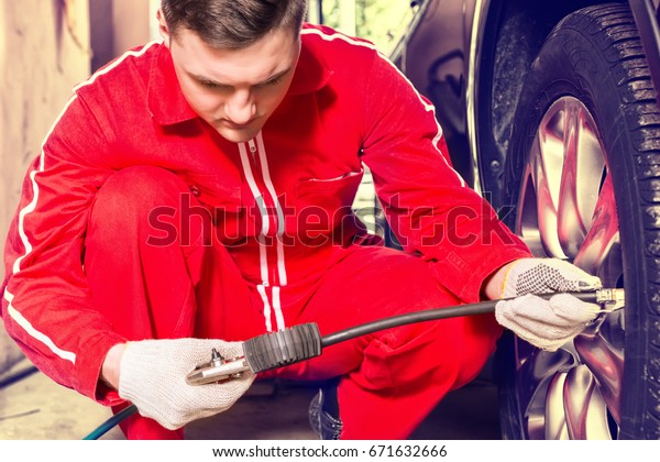 Concentrated motor mechanic checking the air\
pressure of a tyre crouching down alongside the vehicle with the\
gauge from the pump in his gloved\
hand
