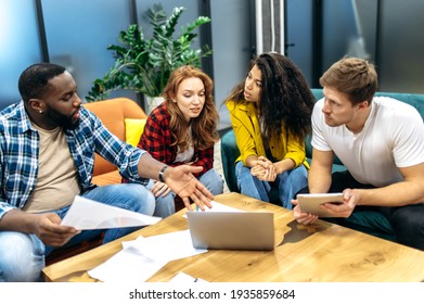 Concentrated Multiracial Business Partners Discussing Corporate Project, Talking About Different Ideas. Young Adult Colleagues Or Students Sitting On The Sofa, Using Laptop, Working Or Study Together