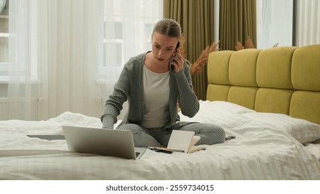 Concentrated multitasking woman girl female student freelancer businesswoman business at home bedroom bed working distant typing laptop computer talking mobile phone call writing notes order delivery - Powered by Shutterstock