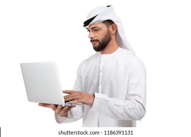 Concentrated on work. Confident young handsome Arab man in kandura working on laptop while standing against white background