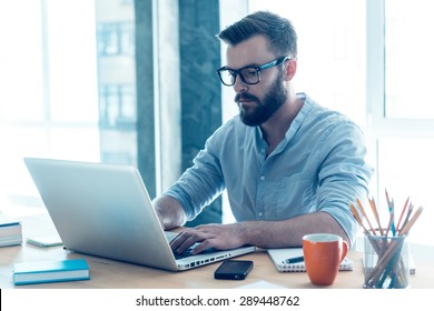 Concentrated on work. Concentrated young beard man working on laptop while sitting at his working place in office - Shutterstock ID 289448762