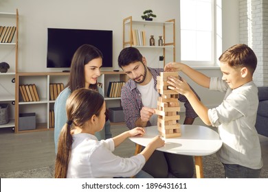 Concentrated Parents And Children Playing Board Game While Enjoying Free Time At Home. Happy Young Caucasian Family With Little Kids Sitting In Sunny Living-room And Taking Blocks From Tumble Tower