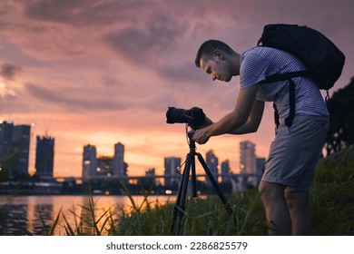 Concentrated photographer with camera on tripod during taking photo of urban skyline. Modern city during beautiful sunset, Singapore.
