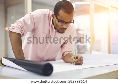 Concentrated professional afro american male engineer drawing outlay of final construction plan as guide for builders with details of plumbing heating electrical ventilation and structural systems 