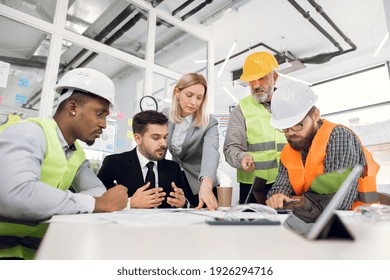 Concentrated Professional Multiracial Team Of Male And Female Engineers Or Architects, Brainstorming Together Over Joint Building Project During Meeting In Office Room