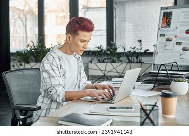 concentrated queer person in casual attire working on laptop near coffee to and smartphone in office - Powered by Shutterstock