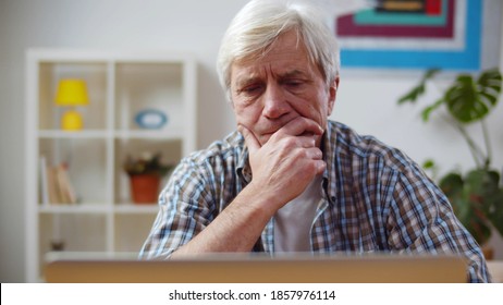 Concentrated Senior Man Using Laptop Sitting In Living Room. Portrait Of Aged Serious Male Working On Computer Remotely Sitting At Home. Retired Man Paying Bills Online