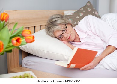 Concentrated Senior Woman Reading Book While Lying In Bed