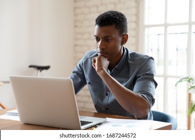 Concentrated serious african ethnicity worker sit in front of laptop reading e-mail feels concerned. Got unpleasant news, search of problem solution, thinking over challenge, fruitful workday concept