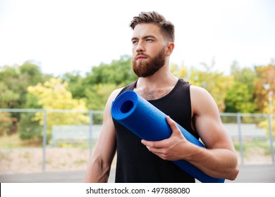 Concentrated Serious Male Yoga Instructor Holding Mat While Standing Outdoors