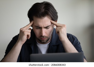 Concentrated serious young employee man holding head, touching templates with fingers with closed eyes, thinking over project issue decision hard, feeling headache, migraine, tiredness, fatigue - Shutterstock ID 2086008343