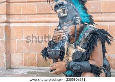 concentrated shaman smelling smoke from a calyx or ritual chalice, aztec dancer with feathered headdress and skulls on his costume, hispanic culture mexican traditional performer