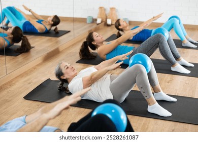 Concentrated sporty senior woman doing crunches with pilates ball during bodyweight workout to strengthen abs and core muscles in fitness studio - Powered by Shutterstock