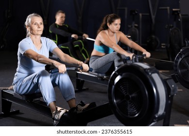 Concentrated sporty senior woman working out on rowing machine during total-body workout in gym. Active lifestyle of older adults concept - Powered by Shutterstock