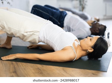 Concentrated sporty young asian woman performing shoulder supported bridge asana Sarvangasana during group workout in yoga studio.. - Powered by Shutterstock